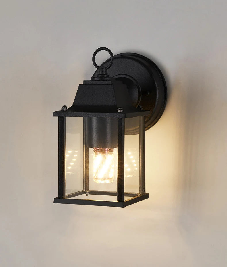 Black outdoor wall lantern light with clear glass panels and warm glowing bulb