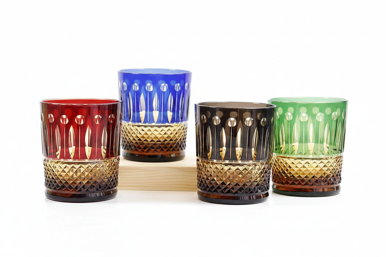 Set of four colored diamond-cut crystal whiskey glasses on a light wooden base