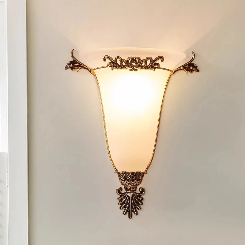 Ornate gold wall sconce with frosted glass shade and decorative metal scrollwork