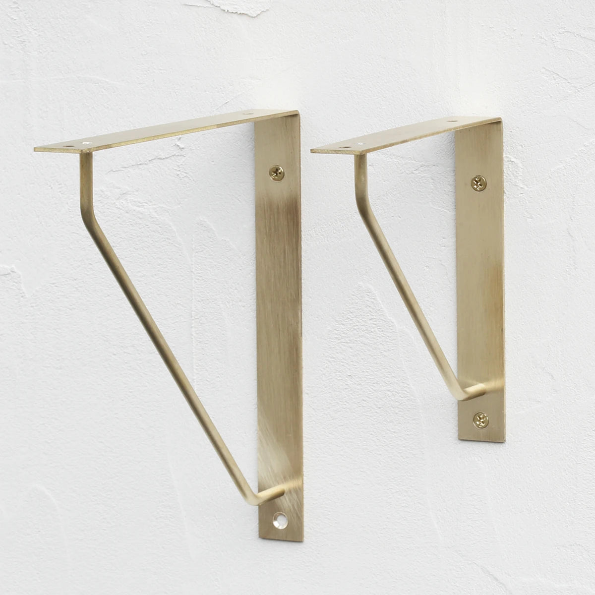 Antique brass triangle shelf bracket pair on wall, curved support arms visible