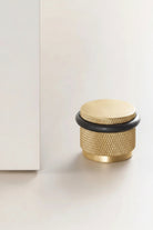Adjustable knurled door stop with brass gold body and black top ring, floor-mounted